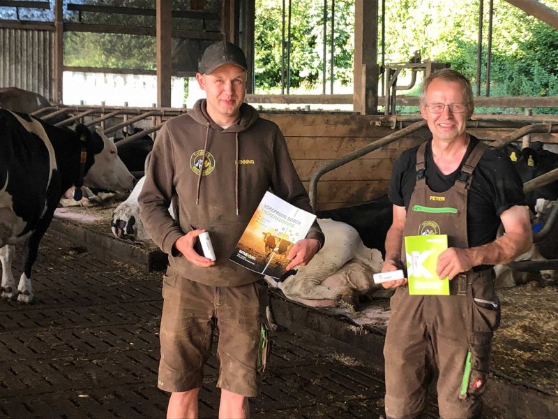 smaXtec testimonial Peter und Henning Thomsen in his barn with information material about smaXtec in their hands